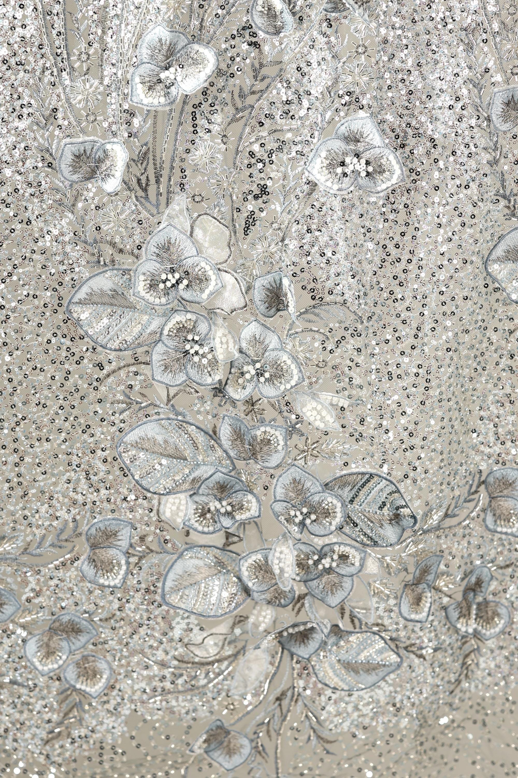 The image is a close-up of a fabric with a floral pattern, featuring a variety of small, intricately designed flowers and leaves in shades of gray and white.