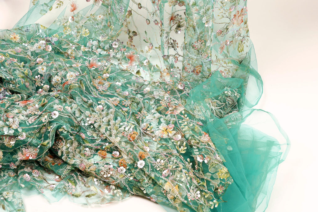 a close-up view of a fabric with a floral pattern, including various shades of green, pink, and white flowers. The fabric appears to be made of sheer material, giving it a delicate and airy appearance.