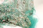 a close-up view of a fabric with a floral pattern, including various shades of green, pink, and white flowers. The fabric appears to be made of sheer material, giving it a delicate and airy appearance.