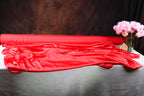a red satin fabric draped over a table, with a vase of pink flowers placed next to it.