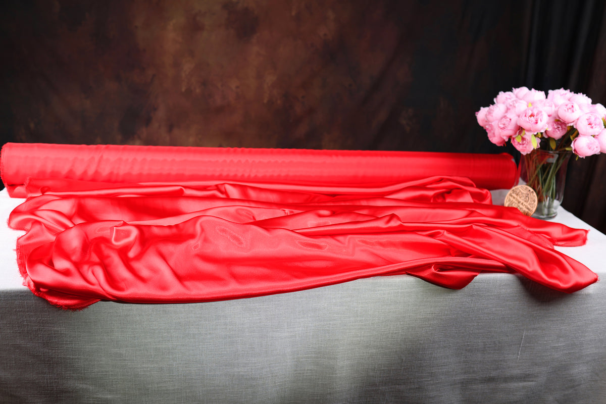 a red satin fabric draped over a table, with a vase of pink flowers placed next to it.