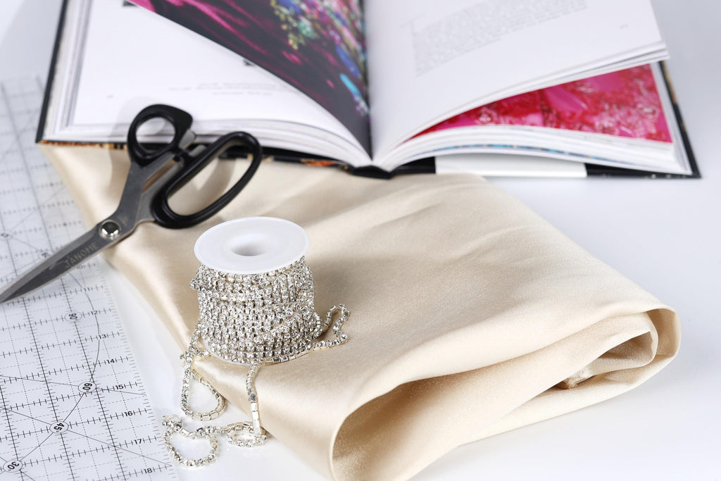 various crafting supplies, including a spool of rhinestone wire, a pair of scissors, and a book with a pink cover.
