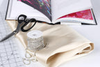 various crafting supplies, including a spool of rhinestone wire, a pair of scissors, and a book with a pink cover.