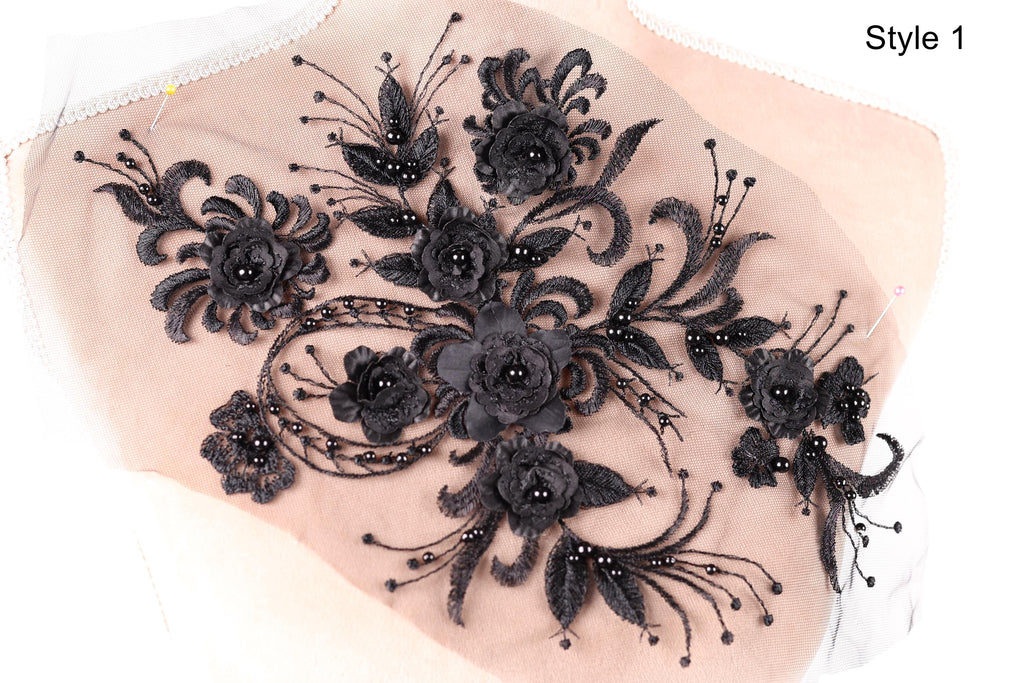 a close-up view of a delicate, intricate black lace design with a floral pattern. The design is composed of numerous black lace flowers and leaves, creating a visually striking and elegant piece of embroidery or textile art.