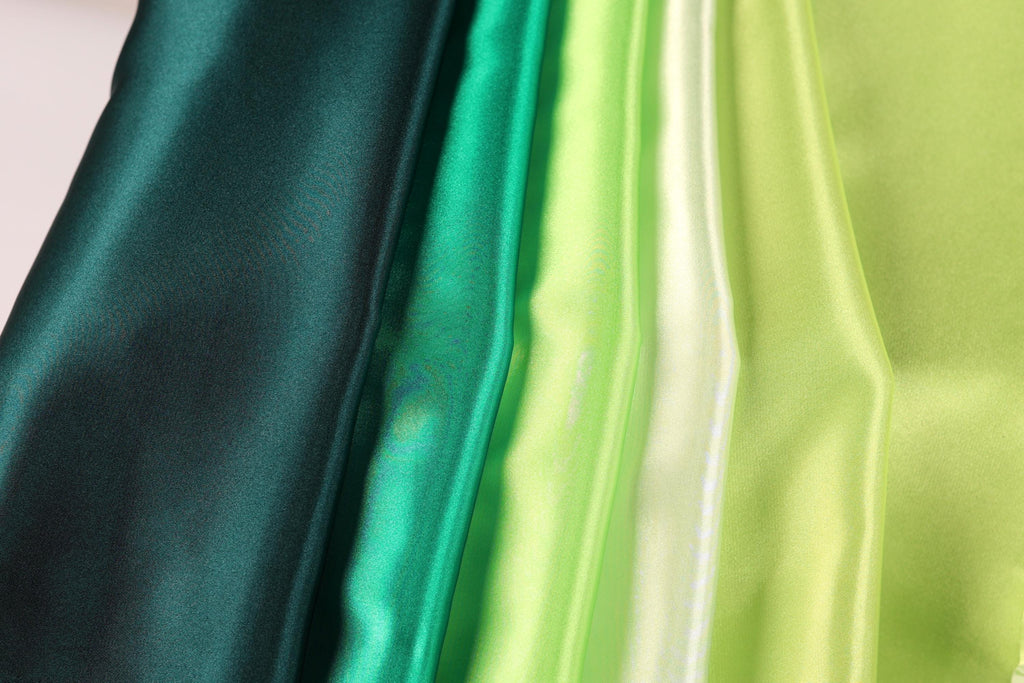 A close-up image of various colored satin fabric, including green, yellow, and dark green, arranged in a vertical line.