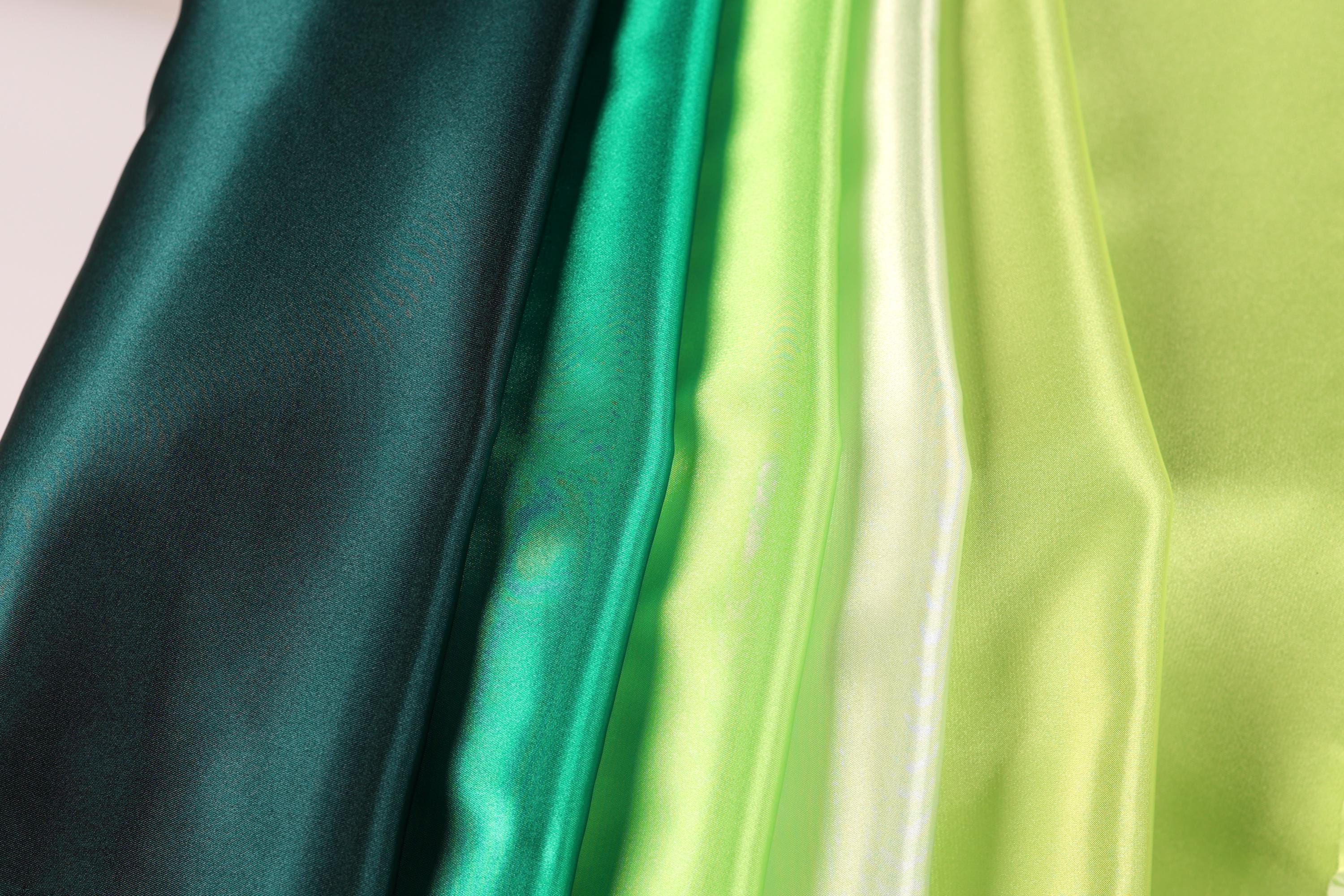 A close-up image of various colored satin fabric, including green, yellow, and dark green, arranged in a vertical line.