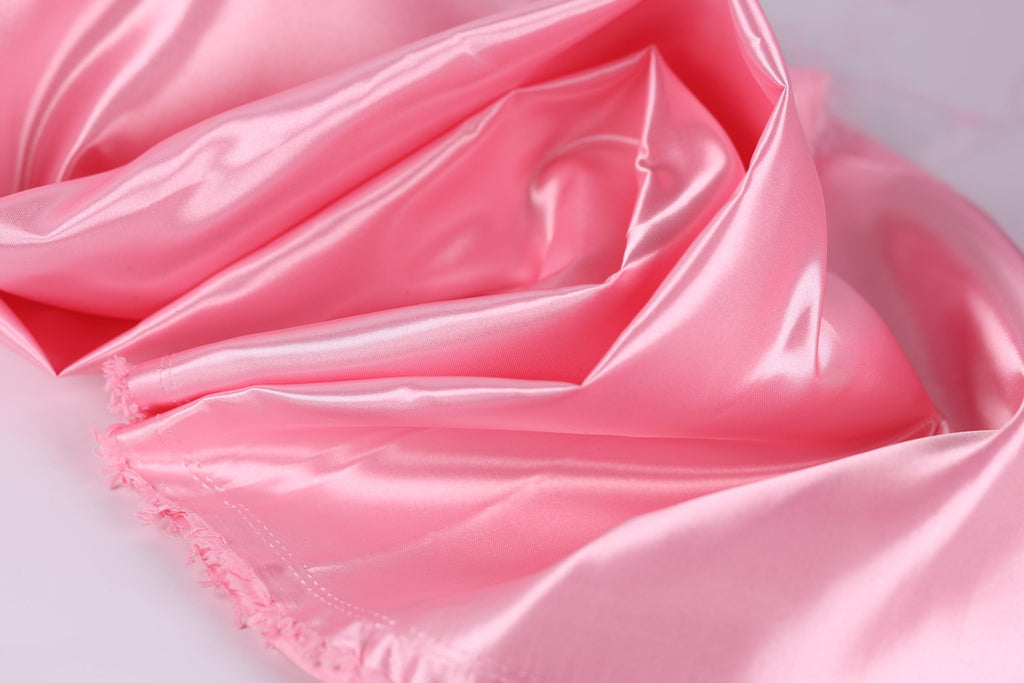A close-up view of a soft, shiny pink satin fabric, with a smooth and flowing texture.