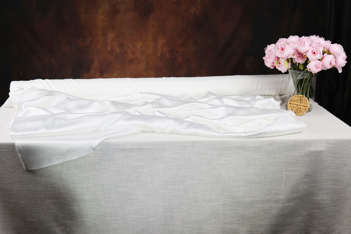 a white tablecloth with a vase of pink flowers placed on it.