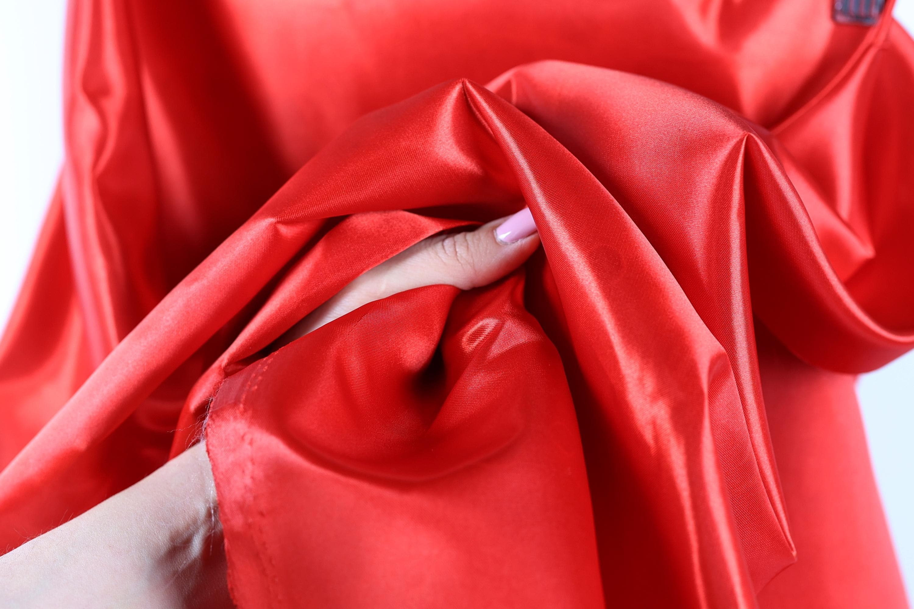 A hand is holding a piece of red satin fabric, with the fabric partially draped over the hand.