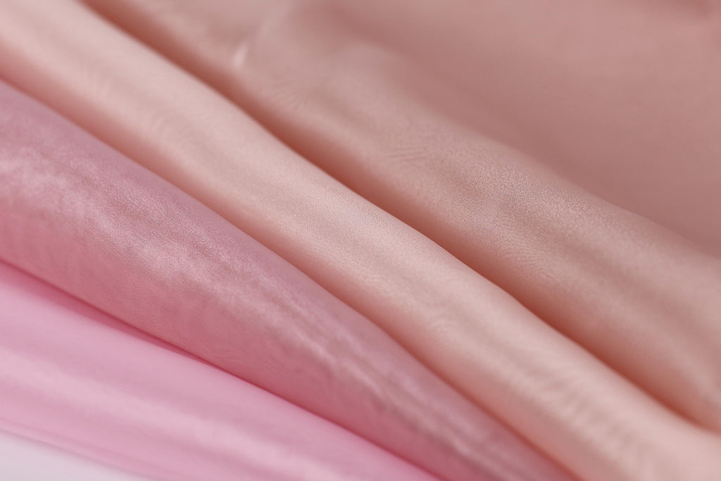 A close-up image of a soft, flowing fabric in shades of pink and peach, with a slightly wrinkled texture.