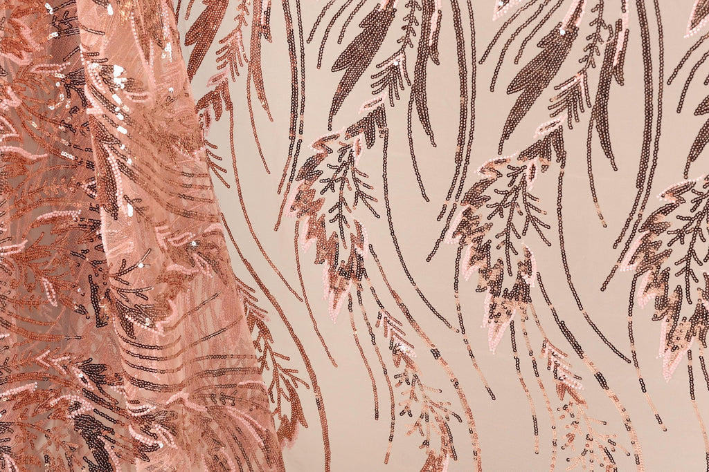 a close-up view of a fabric with a repeating pattern of pink and brown sequin designs. The pattern appears to be a floral or leaf-like design, with the sequins arranged in a way that creates a sense of movement and texture. The fabric is predominantly pink, with some brown elements interspersed throughout the pattern. The image does not contain any text or other discernible objects, and the focus is solely on the intricate and visually appealing design of the fabric.