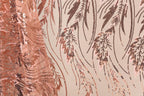 a close-up view of a fabric with a repeating pattern of pink and brown sequin designs. The pattern appears to be a floral or leaf-like design, with the sequins arranged in a way that creates a sense of movement and texture. The fabric is predominantly pink, with some brown elements interspersed throughout the pattern. The image does not contain any text or other discernible objects, and the focus is solely on the intricate and visually appealing design of the fabric.
