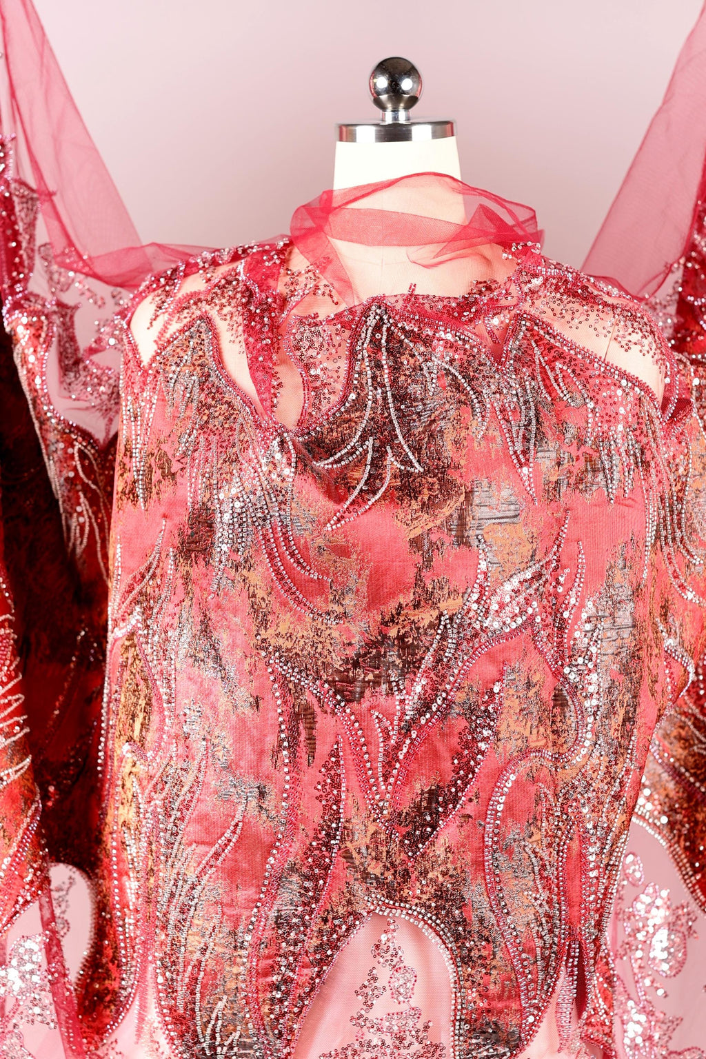 a mannequin wearing a vibrant red and pink dress with intricate beading and embroidery details.