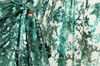 a close-up view of a fabric with a green and blue floral pattern. The fabric appears to be made of sequins or other decorative materials, creating a visually striking and intricate design.