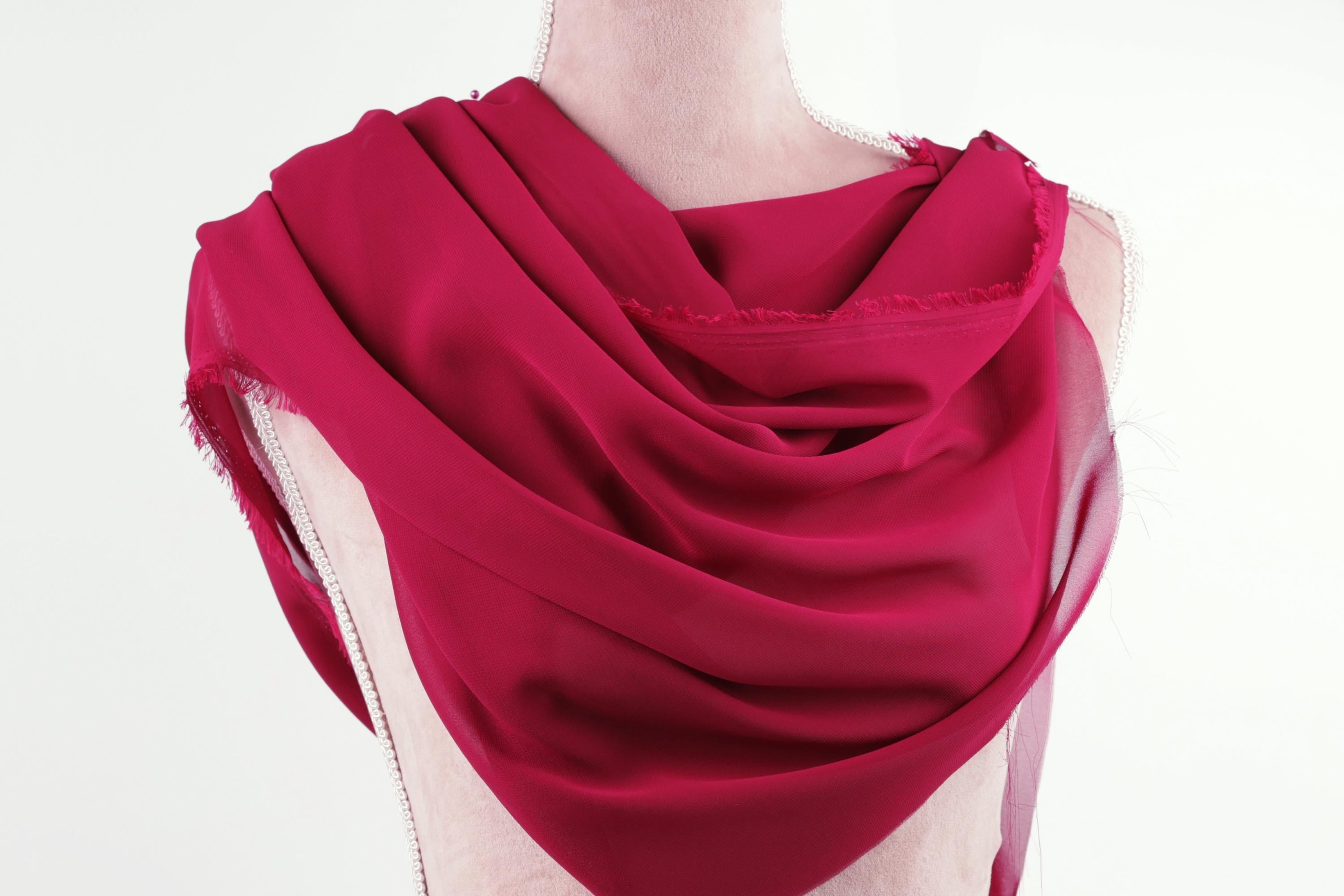 A mannequin wearing a vibrant red scarf draped over its shoulders.
