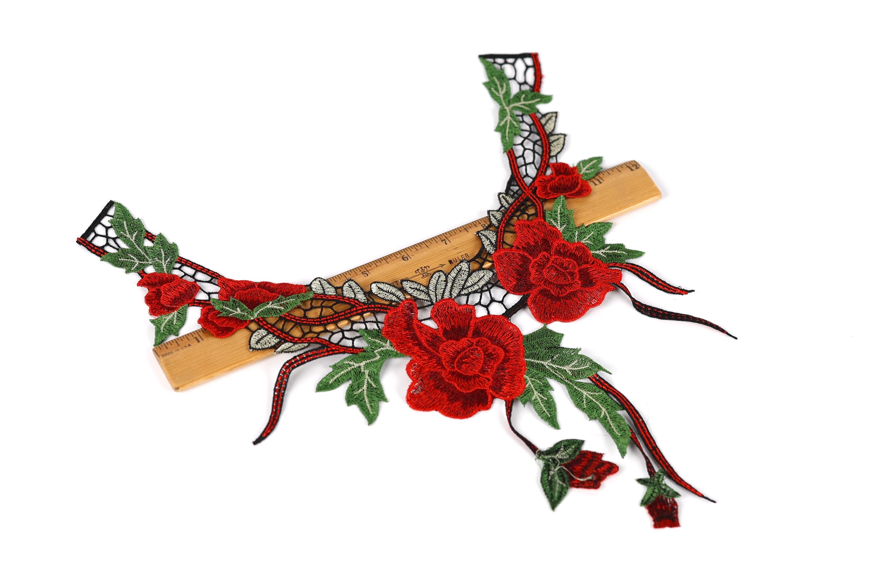 a decorative piece of embroidered fabric with red flowers and green leaves, placed on a wooden ruler for scale.