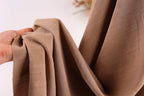 A hand is holding a piece of brown fabric, which appears to be a soft, textured material.