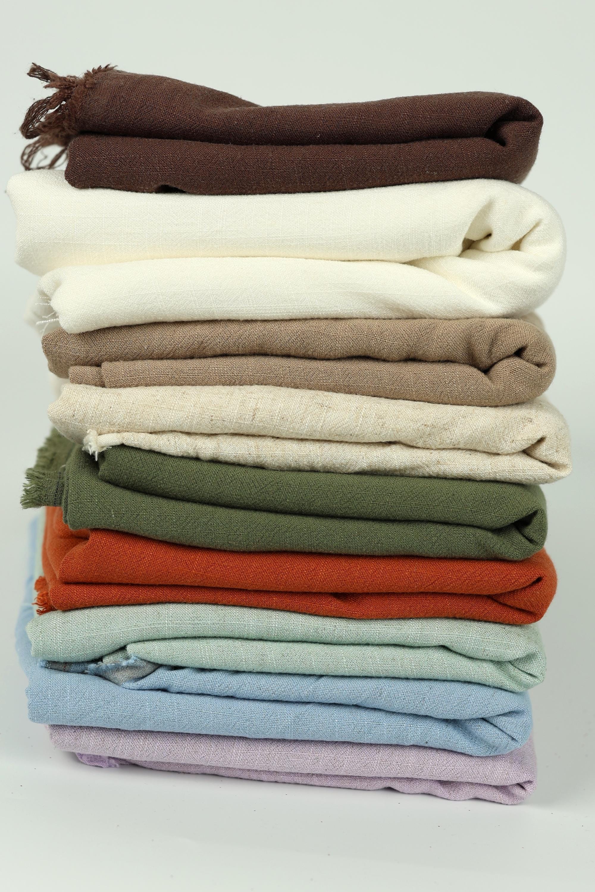 A stack of various colored towels or blankets, including white, brown, green, orange, and purple.