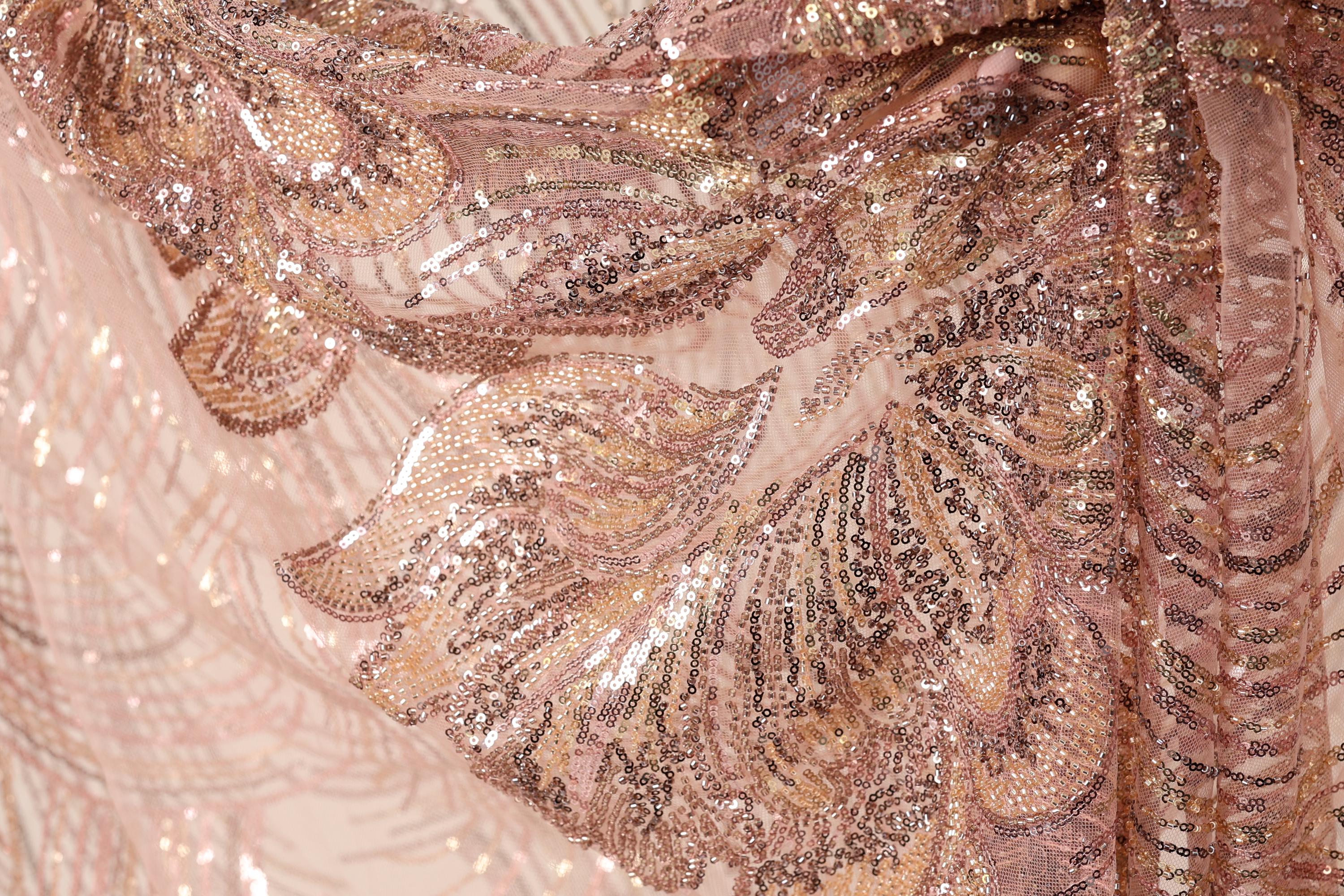 The image is a close-up of a fabric with a pink and gold sequined pattern, featuring a detailed and intricate design.