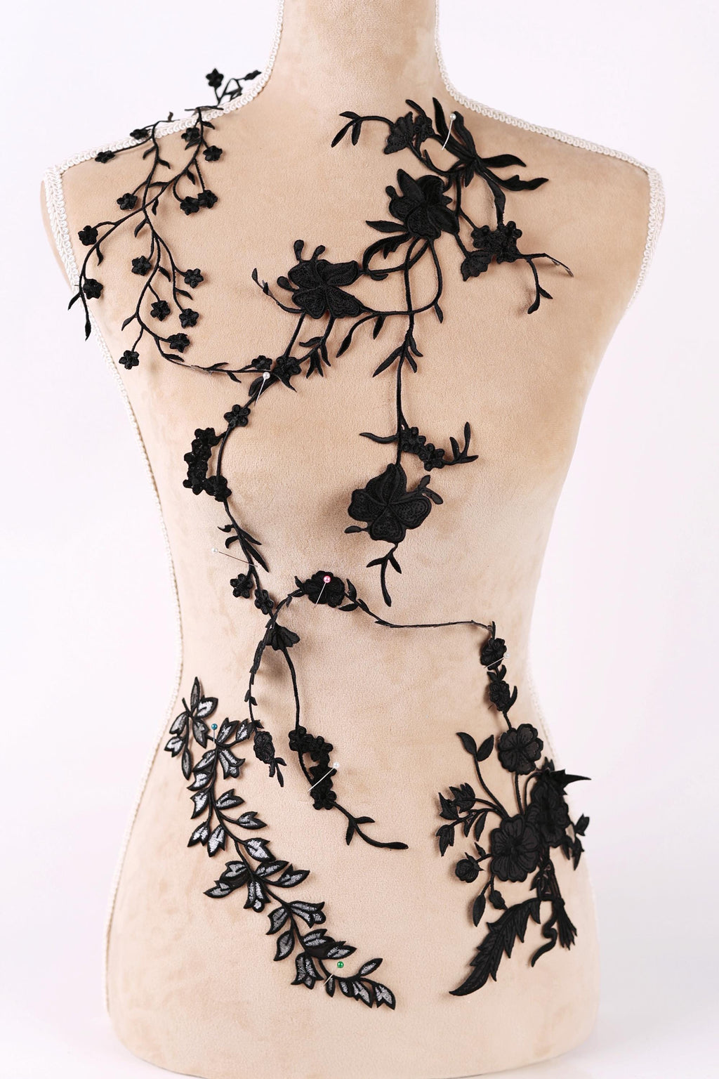 A mannequin torso with black floral embroidery or lace appliques covering it.