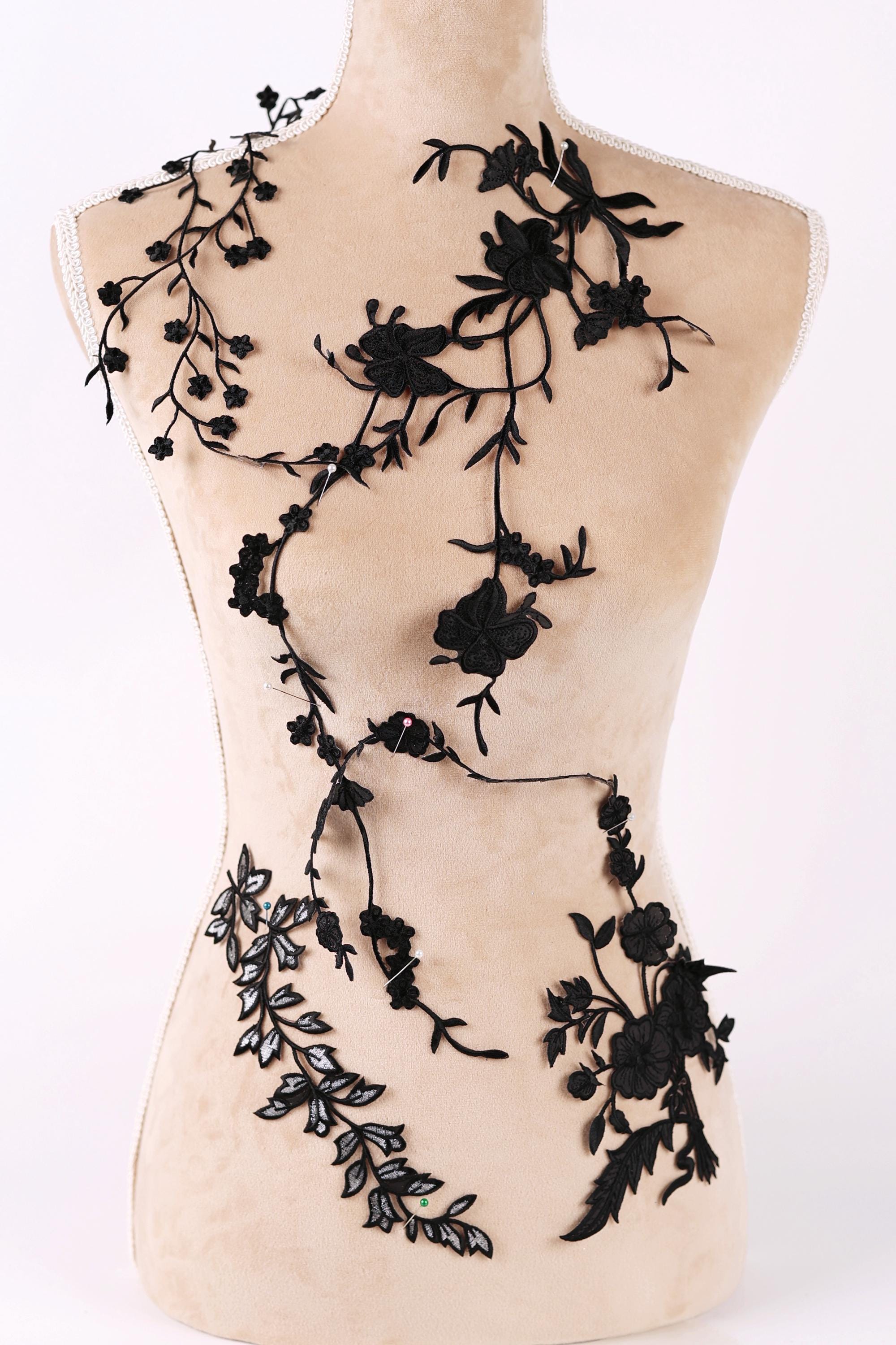 A mannequin torso with black floral embroidery or lace appliques covering it.