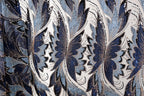 a close-up view of a fabric with a repeating pattern of blue and white flowers or leaves, with some areas of the fabric appearing to be sequined or adorned with glitter.
