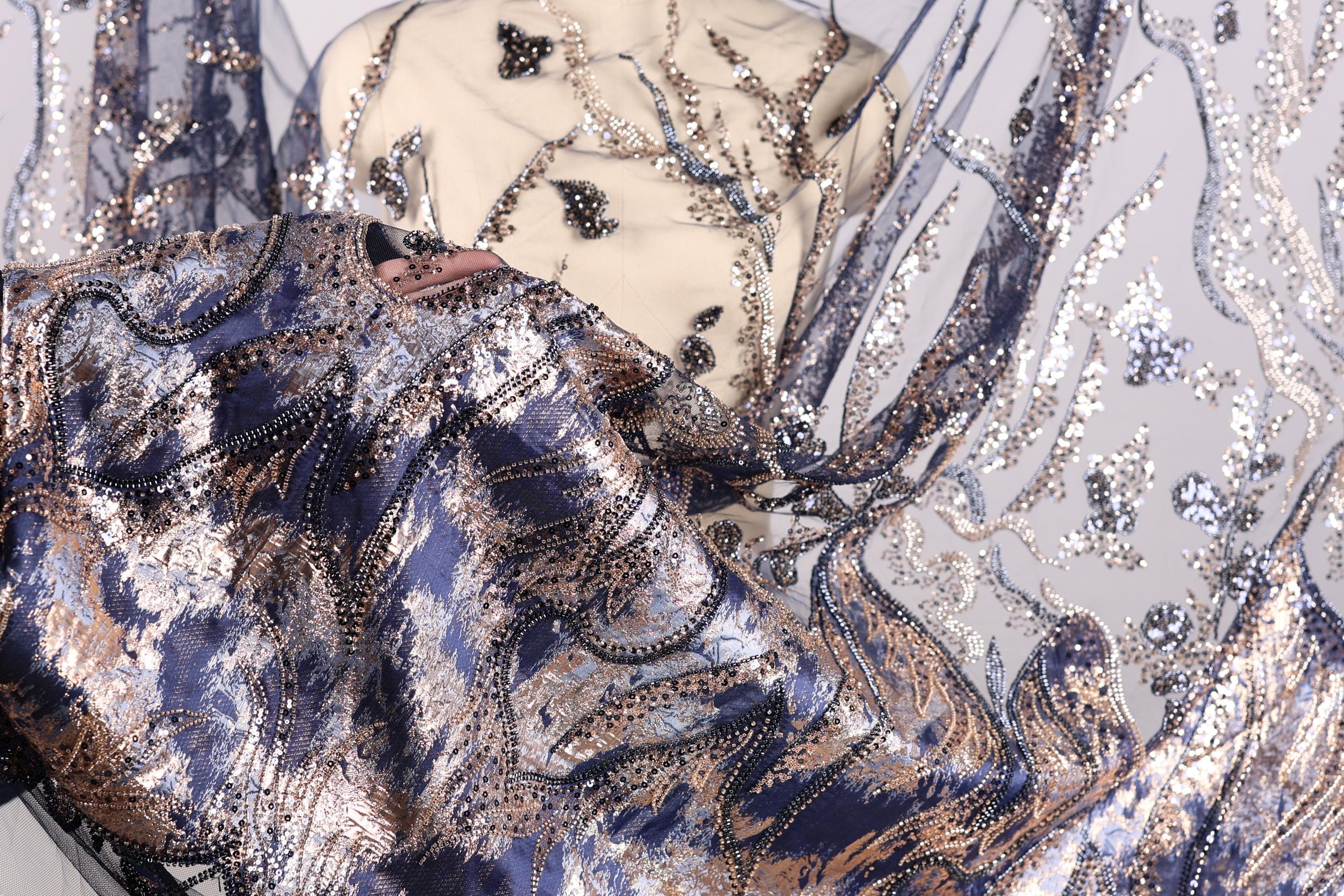 a close-up view of a fabric with a blue and gold pattern, showcasing intricate embroidery and sequin details.