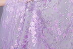 a close-up view of a delicate, lavender-colored fabric adorned with a floral pattern of pink roses and leaves. The fabric appears to be made of sheer material, giving it a soft and delicate appearance.
