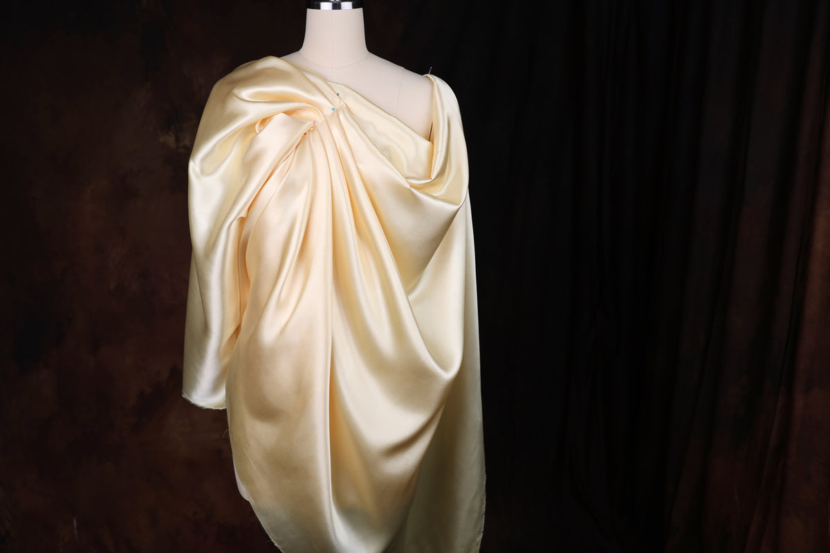 A mannequin wearing a flowing, draped yellow dress against a dark background.