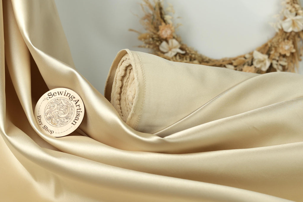 a close-up of a piece of gold satin fabric, with a sewing kit and a wreath in the background.
