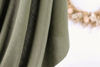 A close-up view of a green fabric with a blurred background featuring dried flowers.