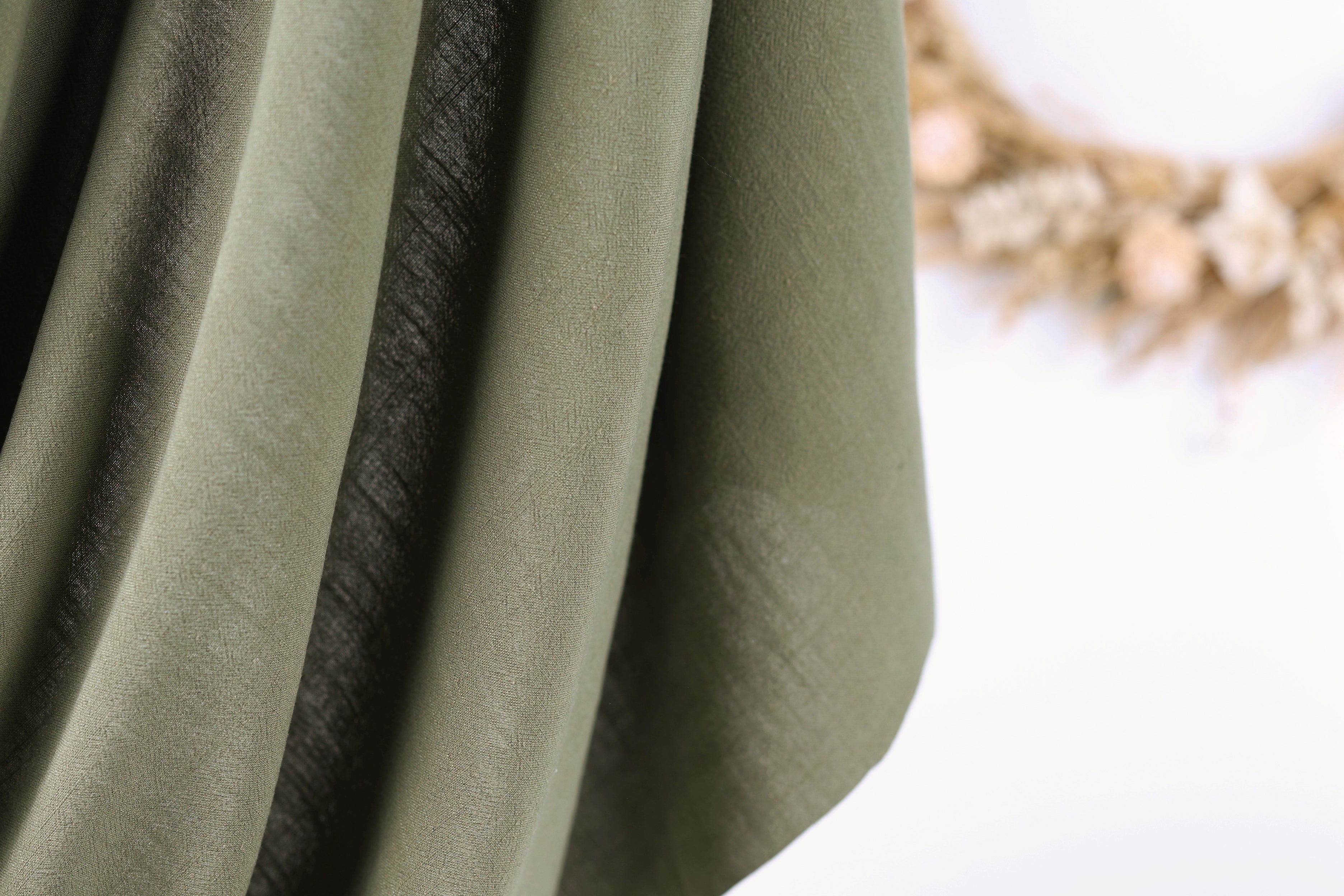 A close-up view of a green fabric with a blurred background featuring dried flowers.