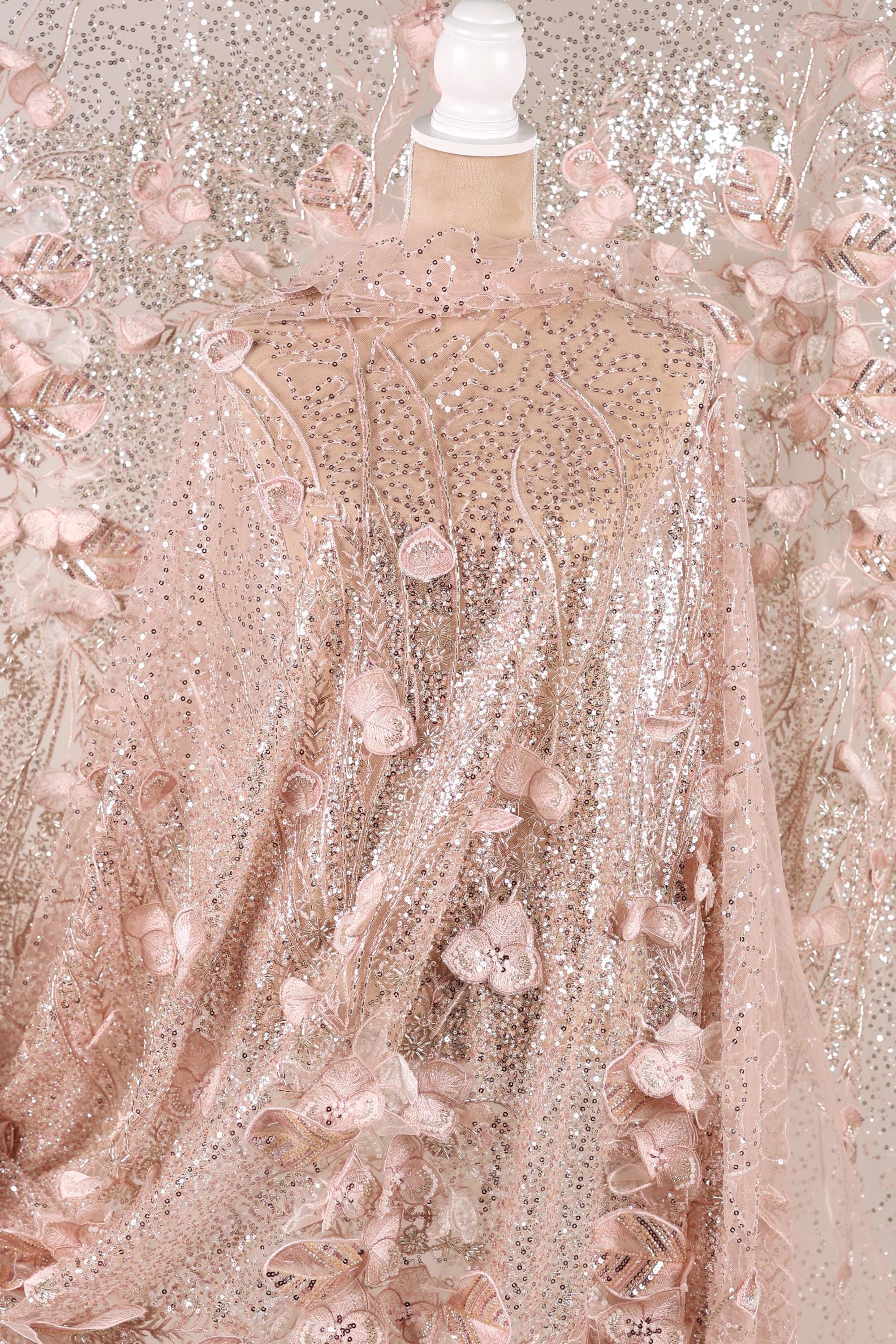 a pink sequin fabric with a floral pattern, including pink flowers and leaves. The fabric appears to be a sheer, sheer fabric with a delicate, lace-like appearance.