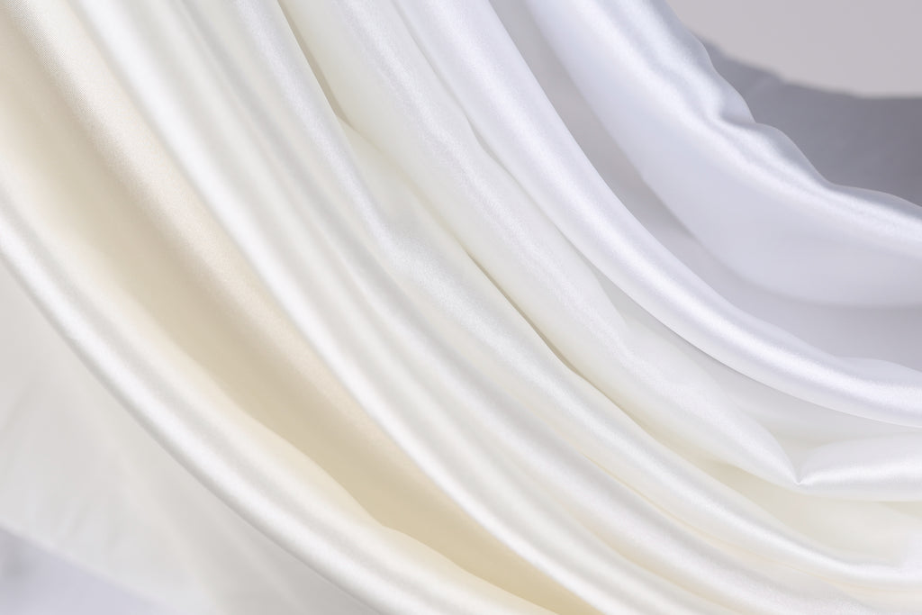The image is a close-up of a fabric with a soft, flowing texture in shades of white and beige.