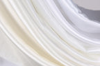 The image is a close-up of a fabric with a soft, flowing texture in shades of white and beige.