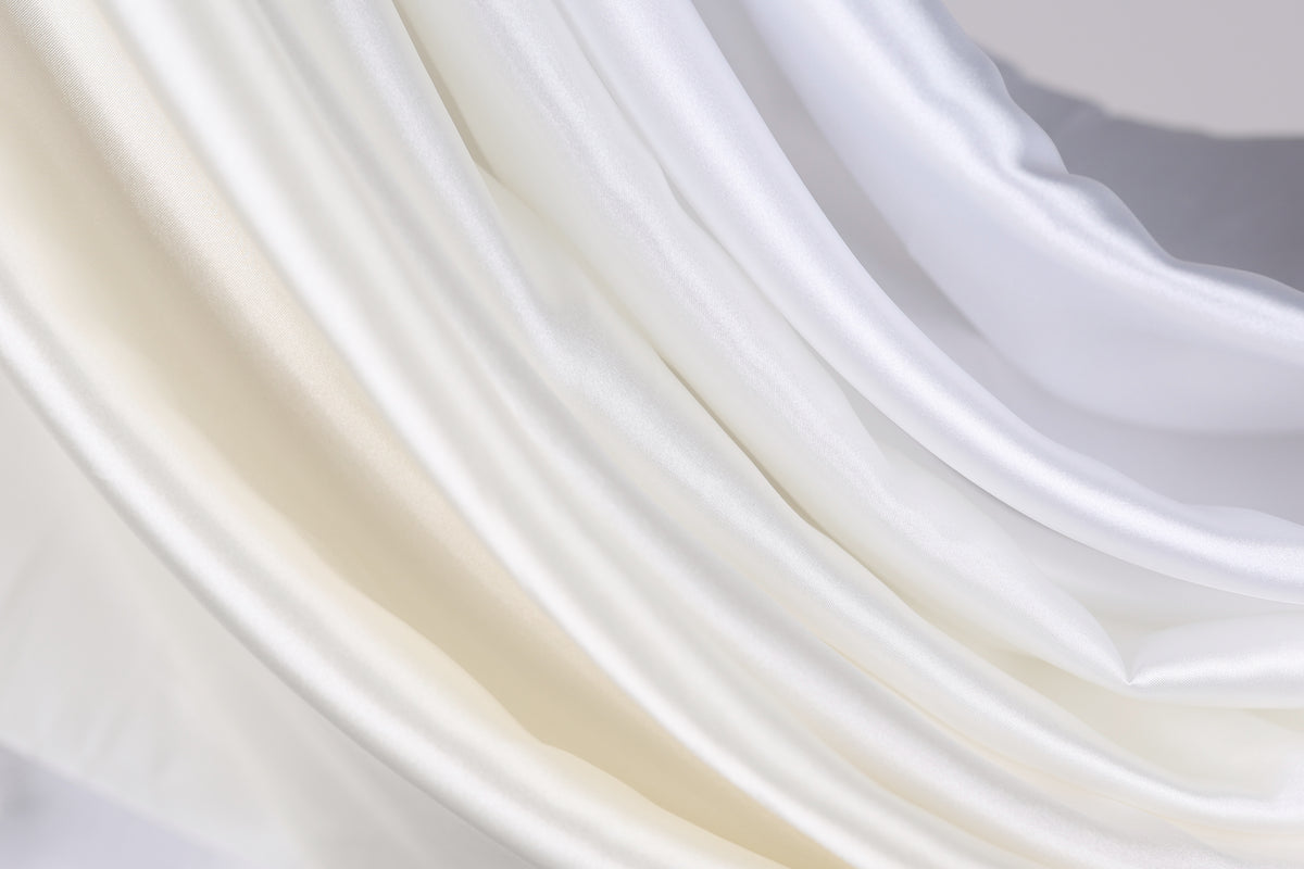 The image is a close-up of a fabric with a soft, flowing texture in shades of white and beige.
