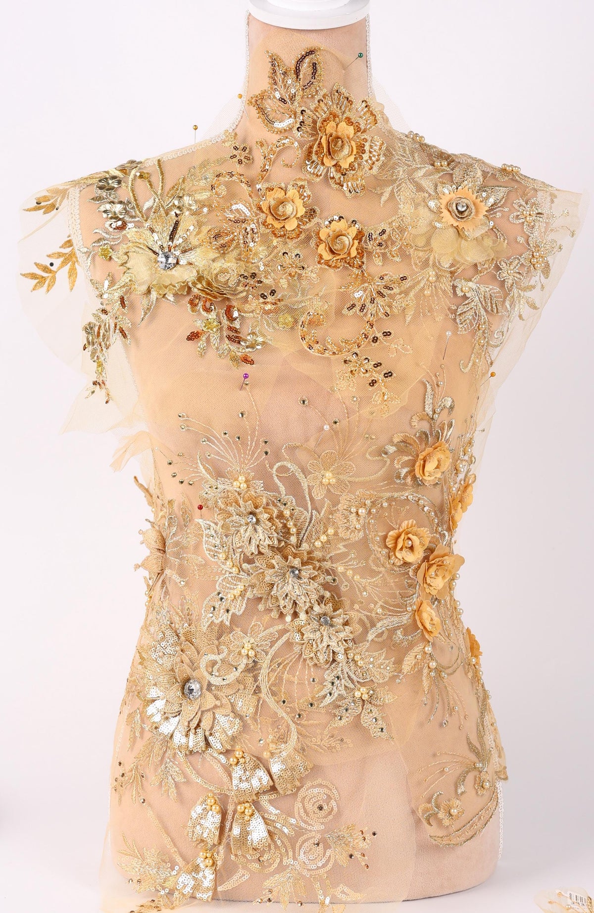 A mannequin wearing an elaborate gold and beige floral dress with intricate embroidery and embellishments.