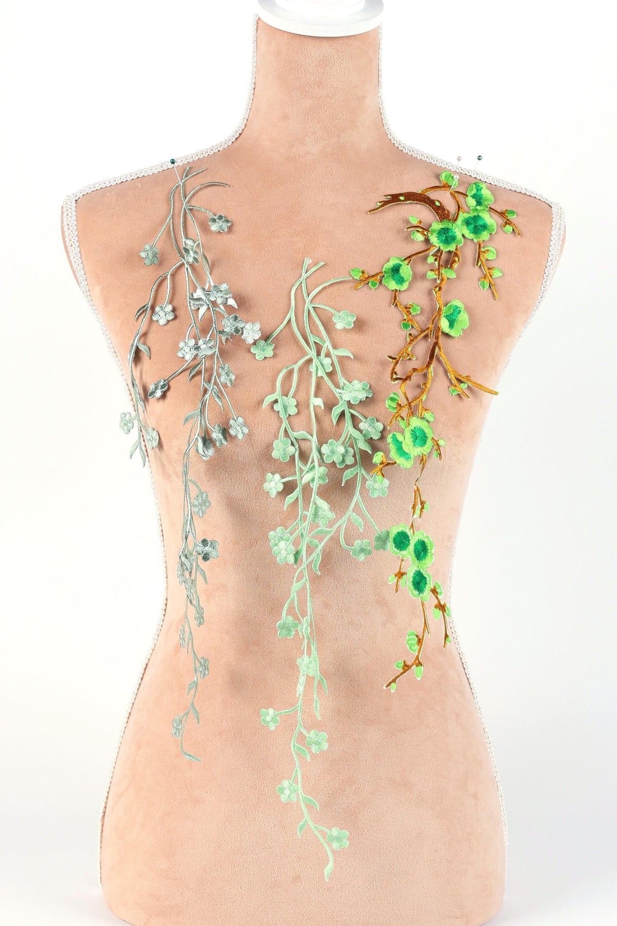 A mannequin torso with three green floral designs on it, including branches with green leaves and flowers.