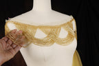 A close-up view of a white bust form with a gold beaded embellishment on the shoulders.