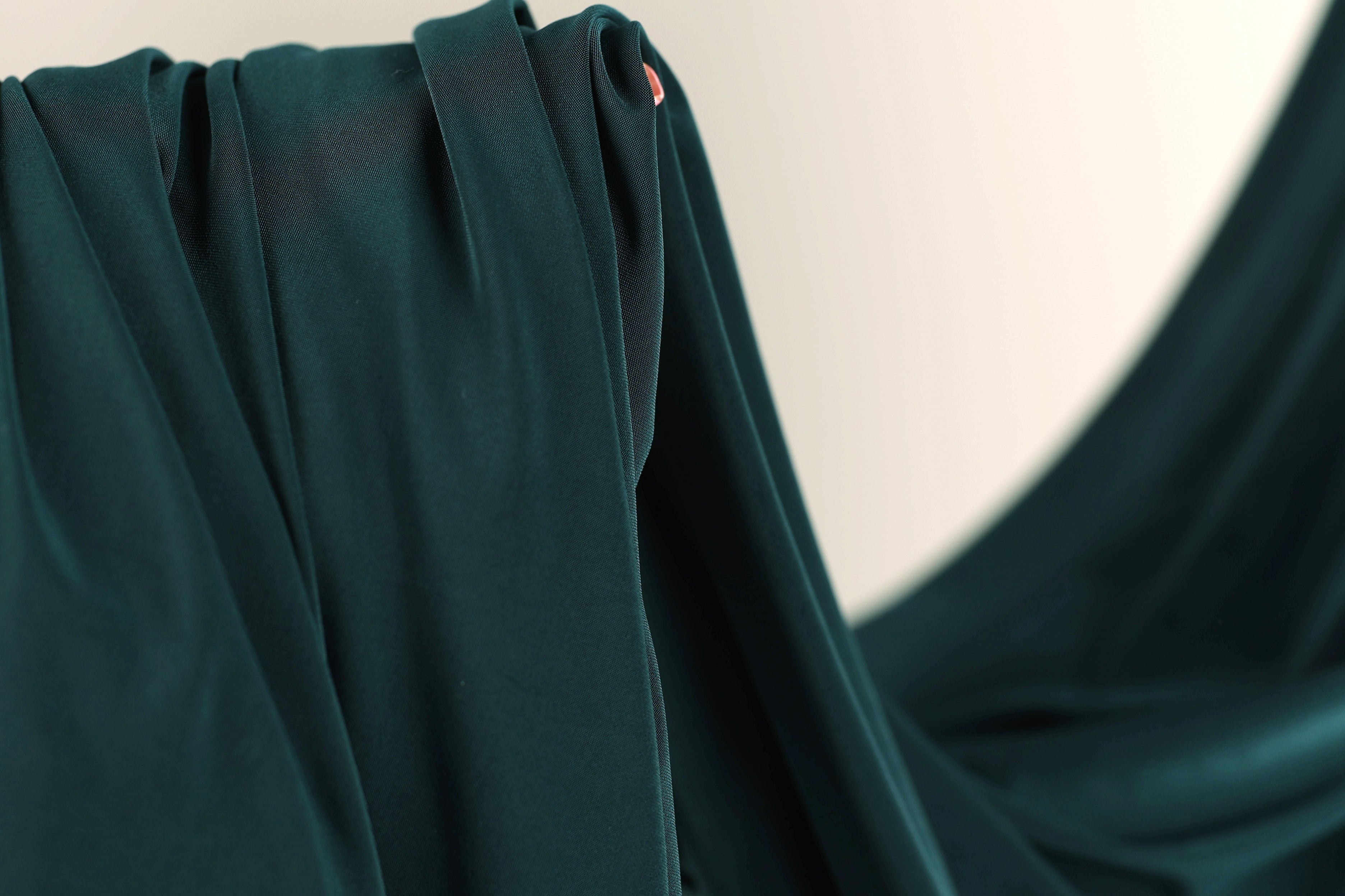 A close-up view of a dark green fabric, possibly silk or chiffon, with a blurred background.