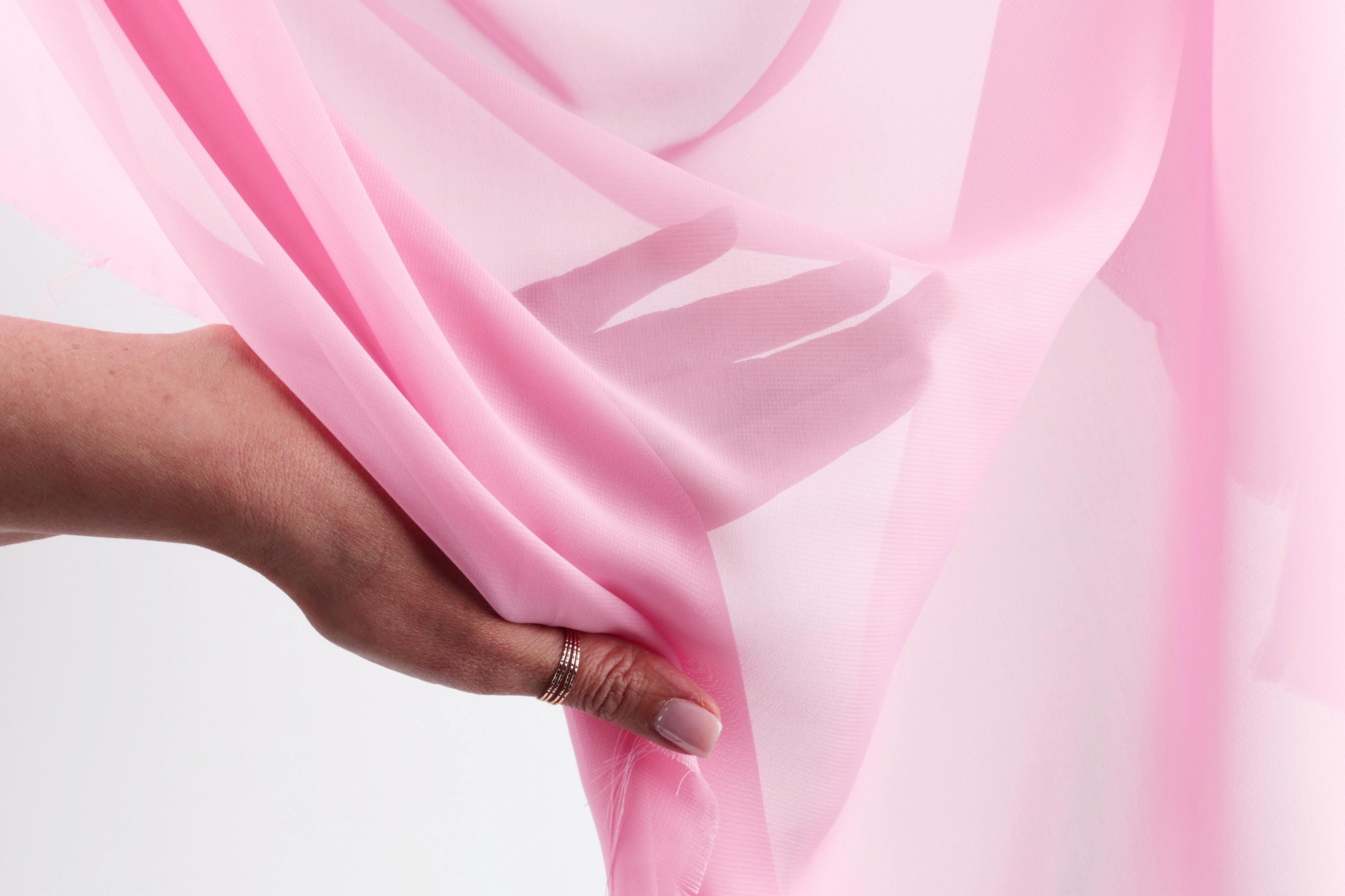 A hand is holding a pink fabric, with the fingers visible and the fabric partially draped over the hand.