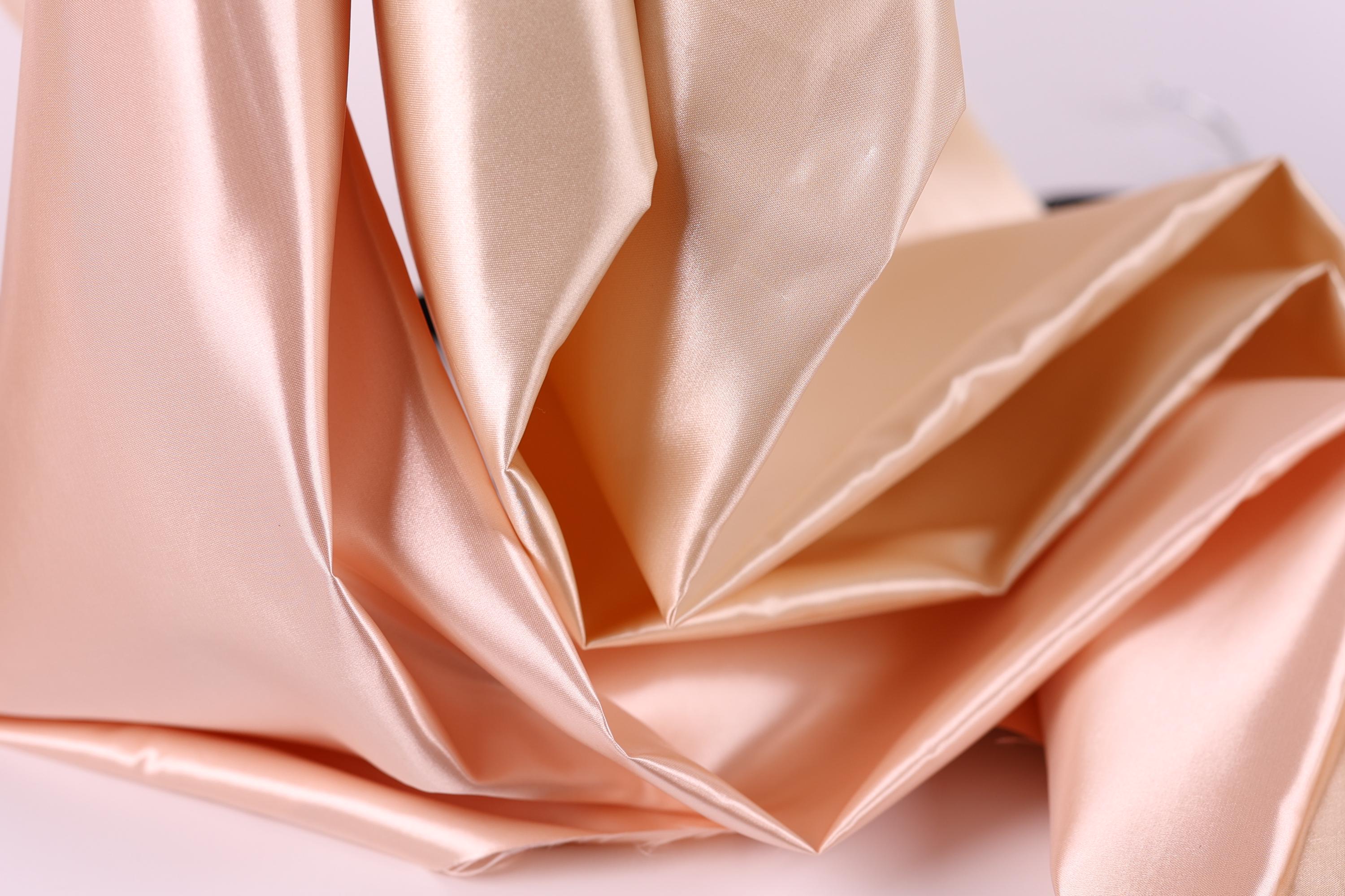 The image is a close-up of a crumpled, light pink satin fabric.