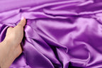 A hand is holding a piece of purple satin fabric, which appears to be soft and smooth.