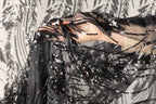 A hand is holding a piece of black and silver sequin fabric, which appears to be a decorative textile.