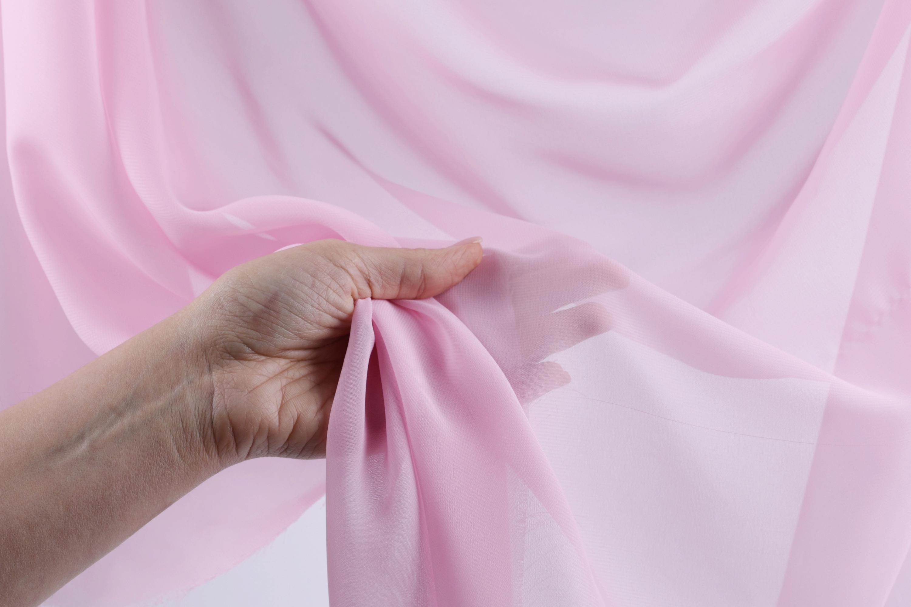 A hand is holding a piece of pink fabric, which appears to be a sheer or sheer-like material.