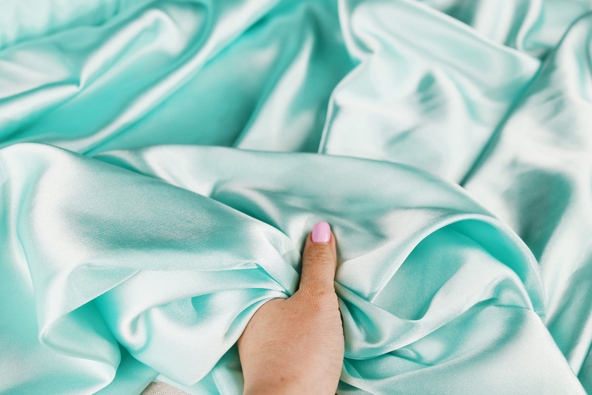 A hand is holding a piece of light blue satin fabric, with the fabric partially covering the hand.