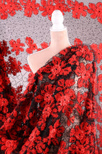 a close-up view of a fabric with a striking red floral pattern. The fabric appears to be a sheer material, with a black and red floral design that creates a visually appealing contrast. The fabric is spread out, revealing its intricate details and the vibrant colors of the red flowers.