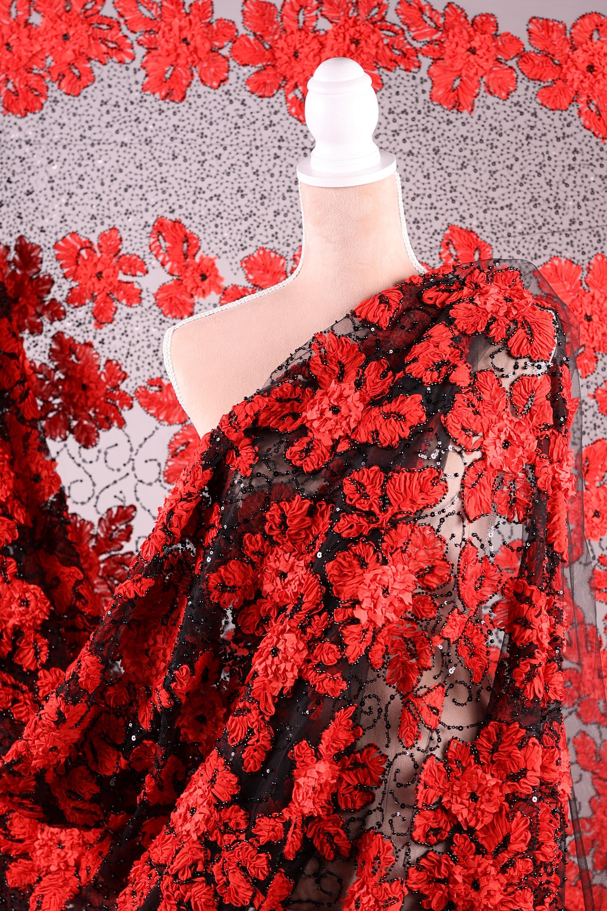 a close-up view of a fabric with a striking red floral pattern. The fabric appears to be a sheer material, with a black and red floral design that creates a visually appealing contrast. The fabric is spread out, revealing its intricate details and the vibrant colors of the red flowers.