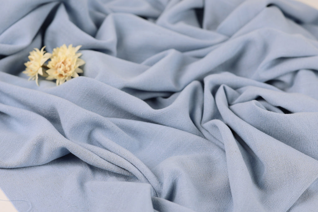 a close-up view of a crumpled light blue fabric, with a small yellow flower resting on top of it.
