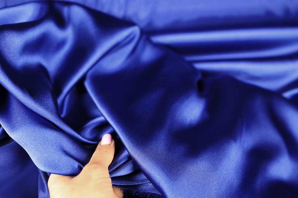 A hand is holding a piece of blue satin fabric, which appears to be a close-up view of the material.